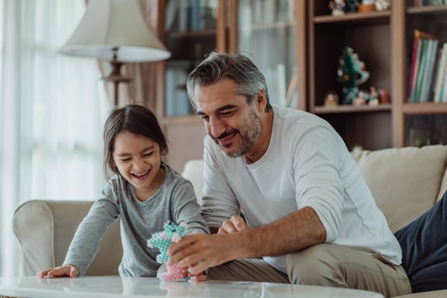 Man and child smiling while building a colorful toy together on a living room table